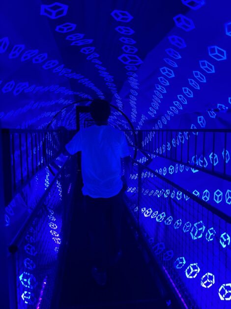 A teen walking through a dark and creepy neon tunnel at the Museum of Illusions St. Louis.